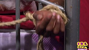 a woman in a nightgown performs oral on a bound man in a femdom scene.